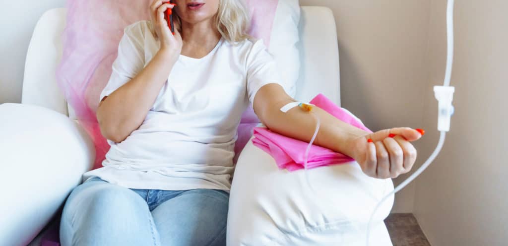 Woman in Hospital Talking at Mobile Phone While IV Drip Needle is in her Arm | Cloud 9 MedSpa in Casa Grande, AZ