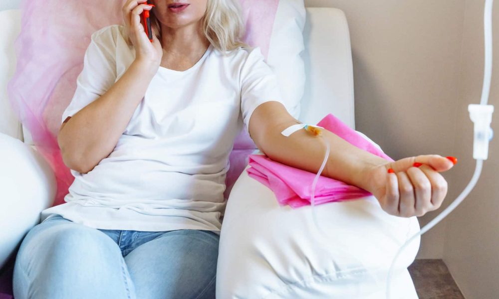 Woman in Hospital Talking at Mobile Phone While IV Drip Needle is in her Arm | Cloud 9 MedSpa in Casa Grande, AZ